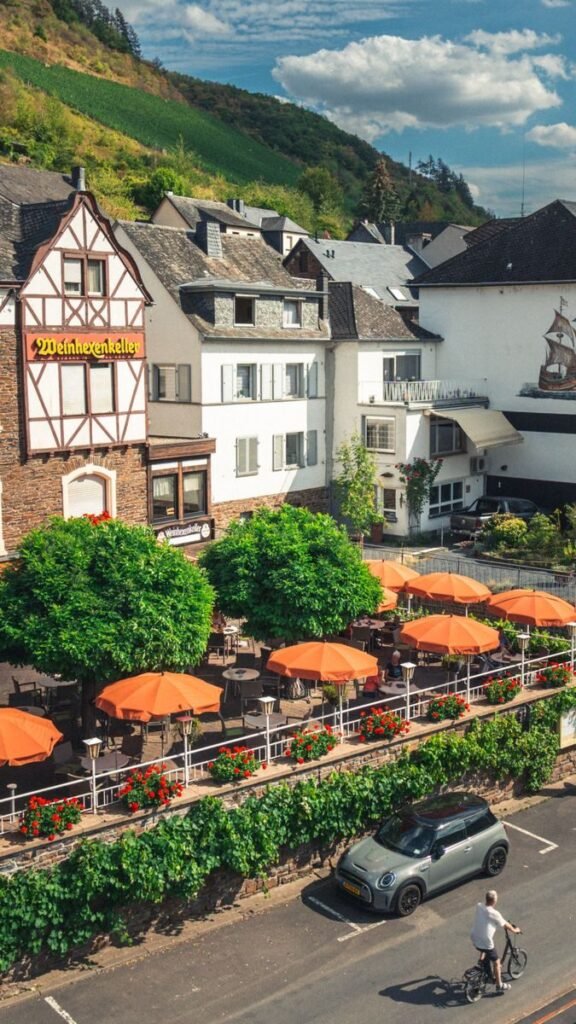 A picturesque street view of Cochem, Germany showcasing traditional architecture, a cafe, and a cyclist.