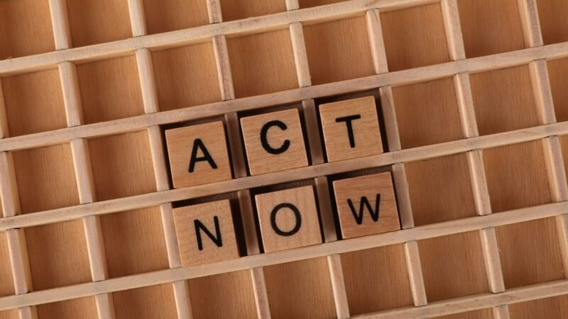 Wooden letter tiles forming the phrase 'Act Now' on a wooden grid background.